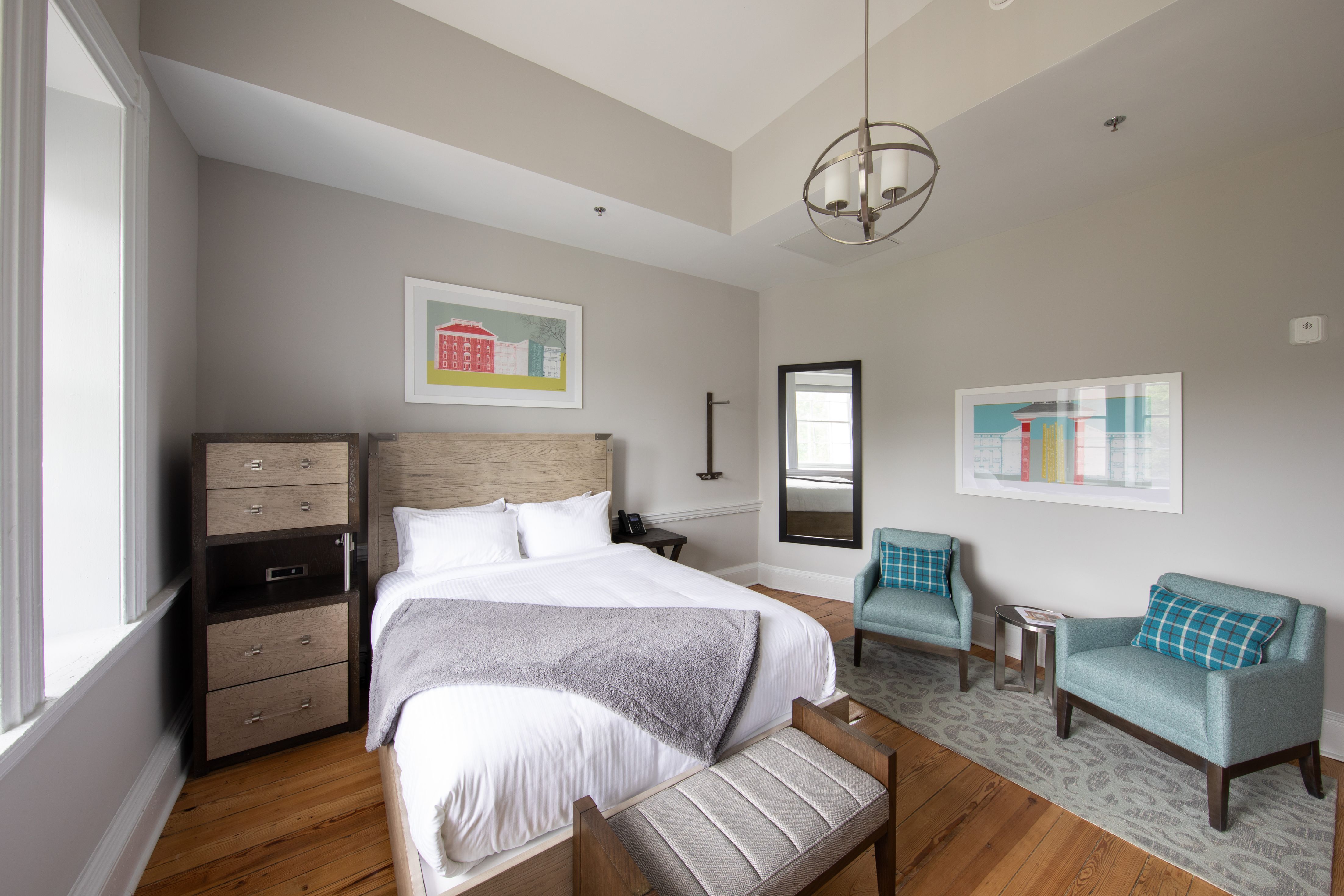 Image of Deluxe Queen Guestroom with Queen-sized bed, accent chair, and wall mirror. The Blackburn Inn & Conference Center, a member of Historic Hotels since 2018, dates to 1828. It is located in Staunton, Virginia.